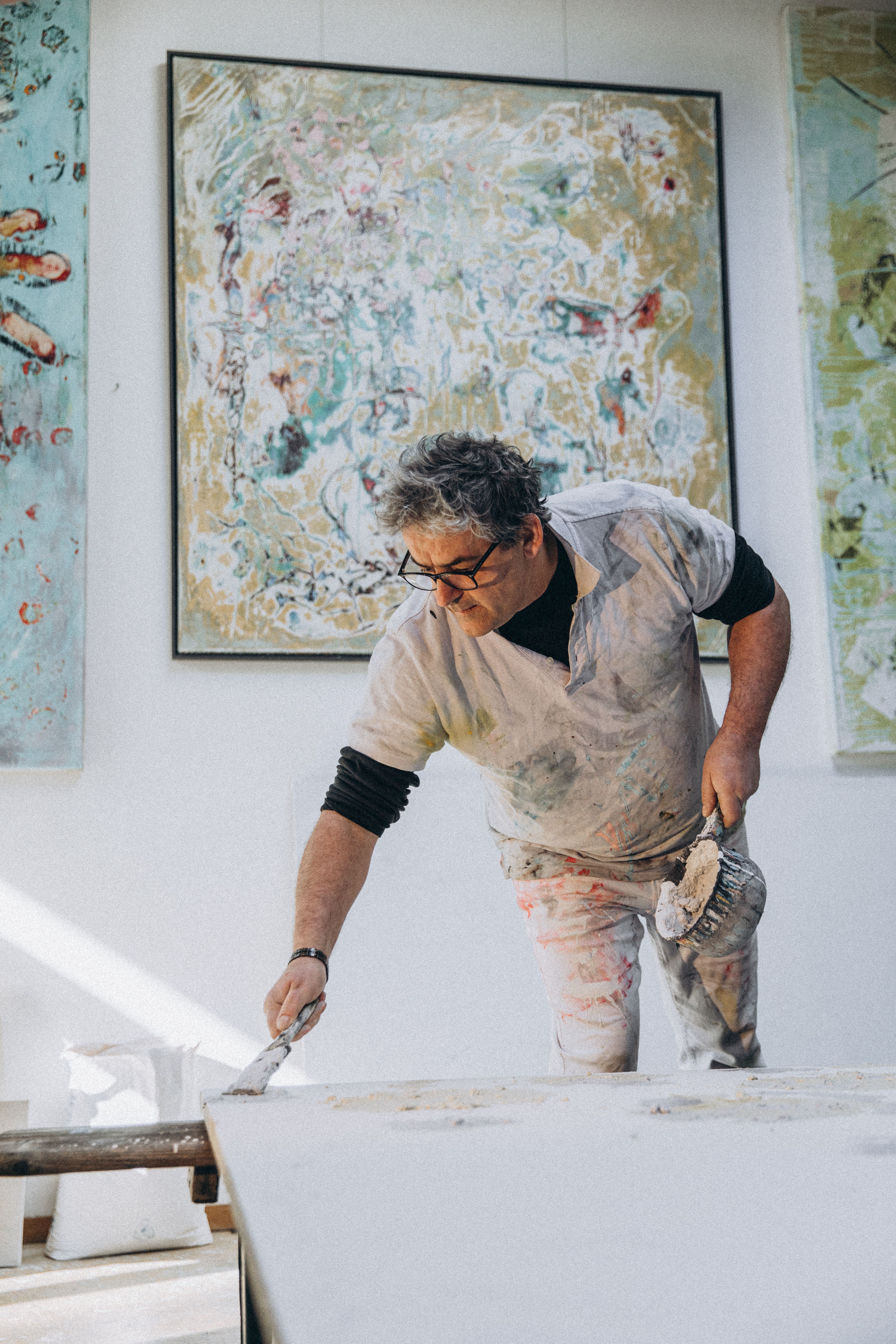 Elderly artist intensely working on a painting in a bright, artistic studio space.