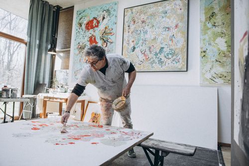 Free A male artist immersed in painting inside a sunlit studio filled with his artwork. Stock Photo