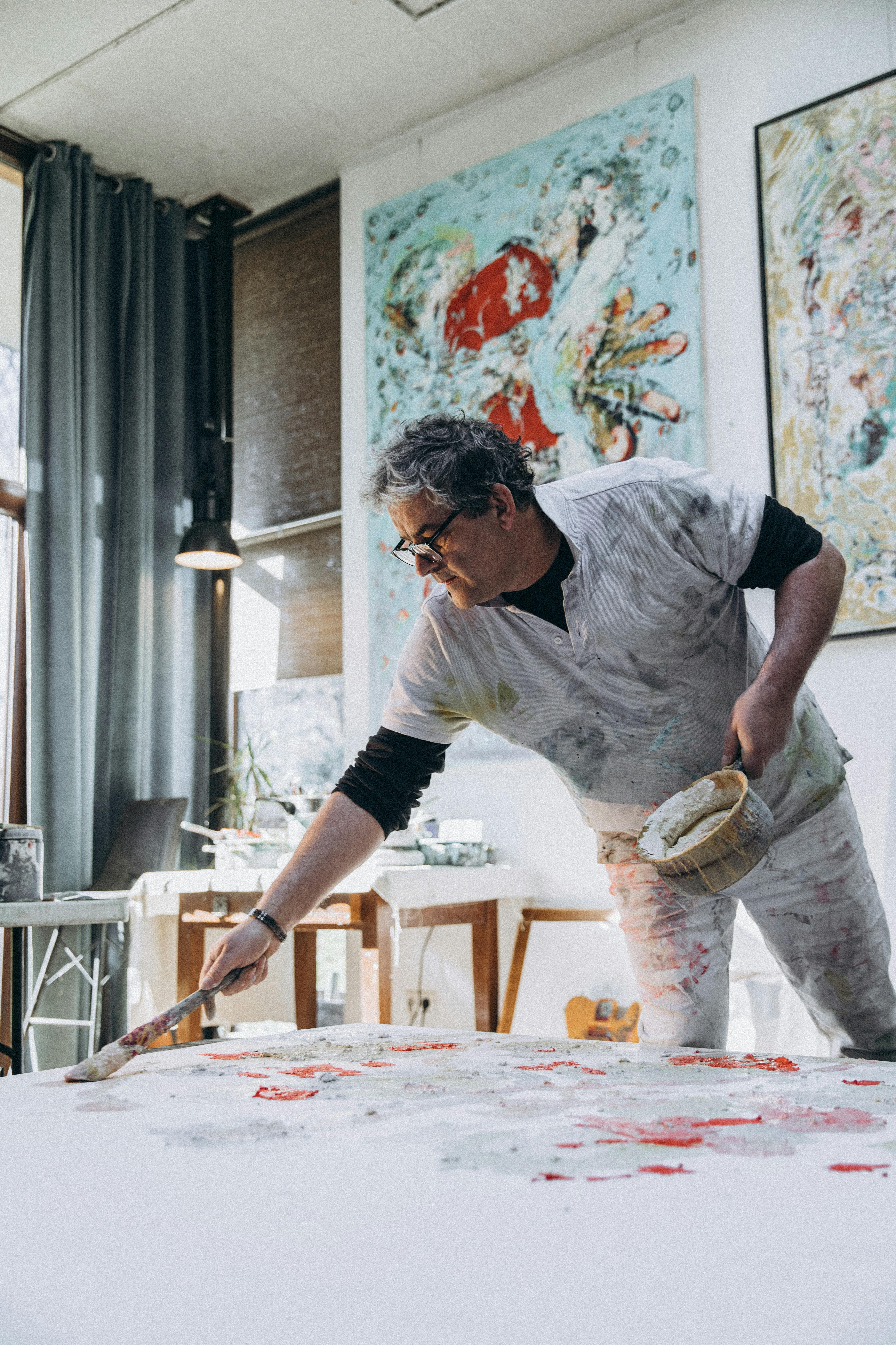 A male artist passionately paints in a bright and airy studio space.