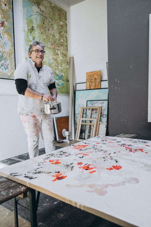 A woman in white pants and a white shirt is painting on a table