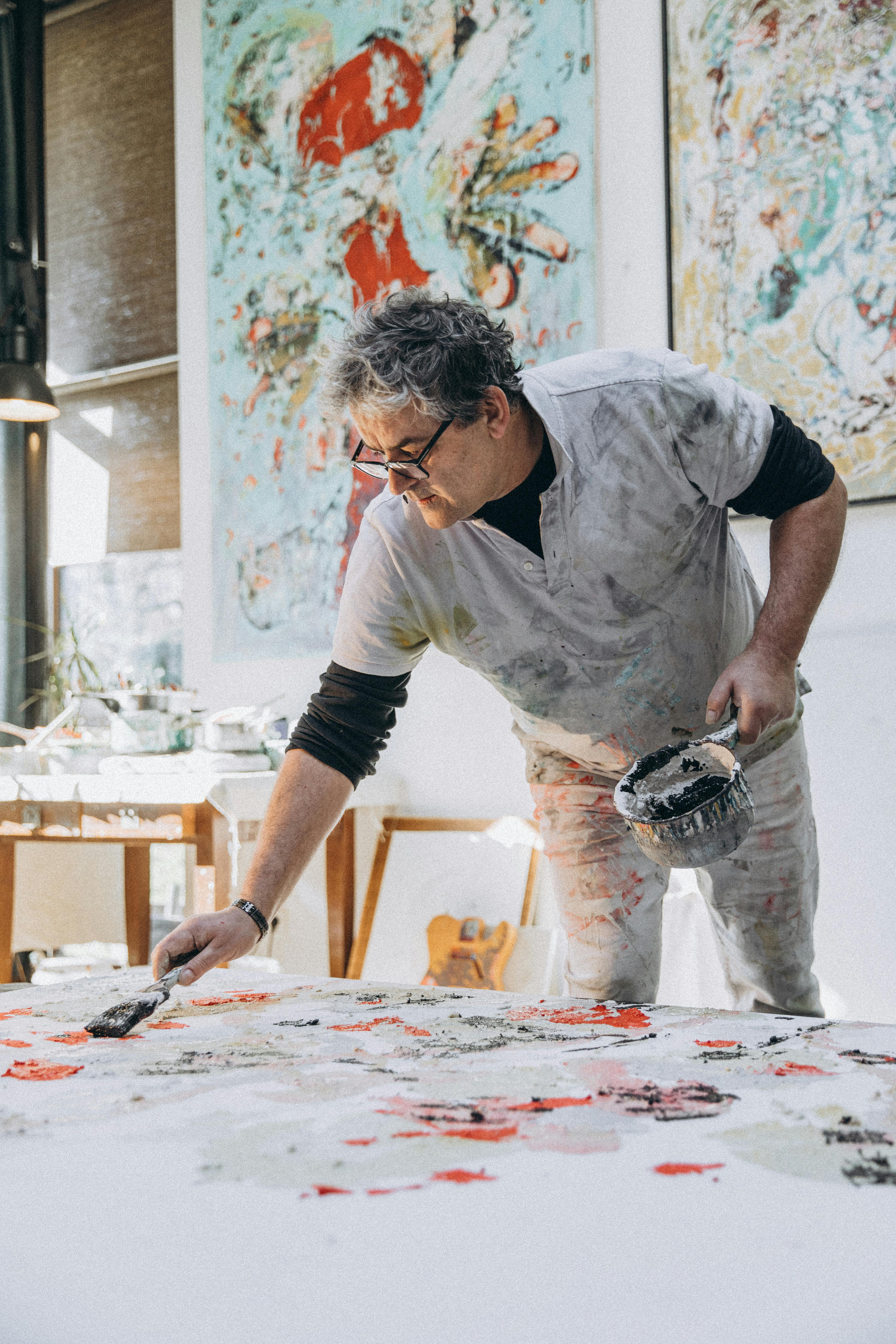 An artist intently works on an abstract painting in a bright studio setting.