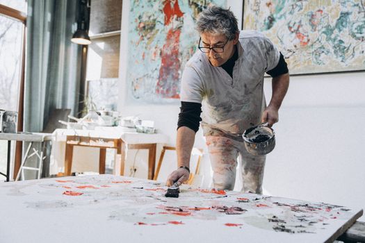 Adult male artist creating abstract artwork in a well-lit studio space, working passionately on a large canvas.