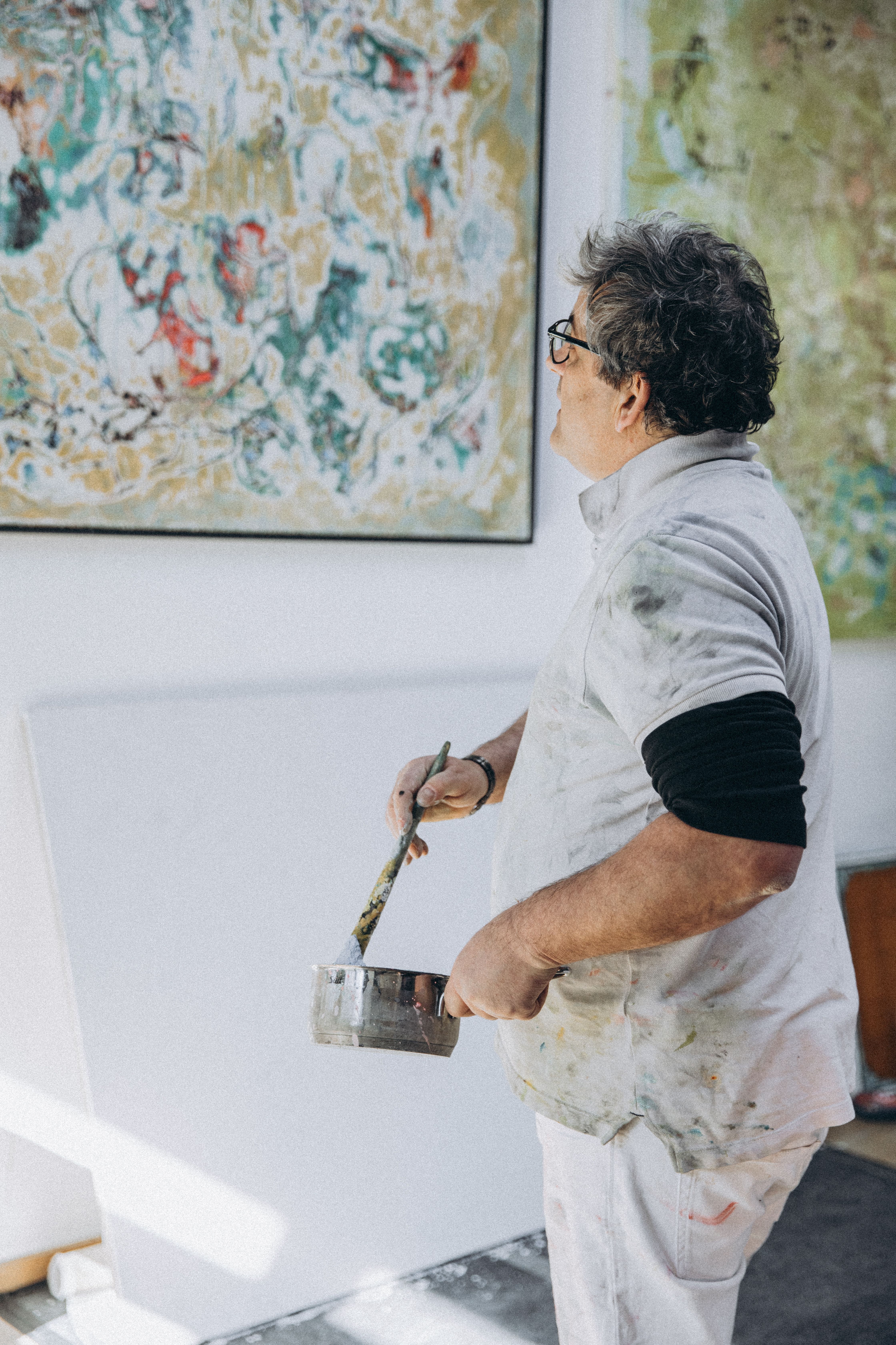 Elderly male artist painting an abstract canvas in a sunlit studio setting.