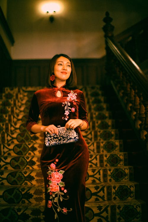 A woman in a velvet dress and floral clutch standing on stairs