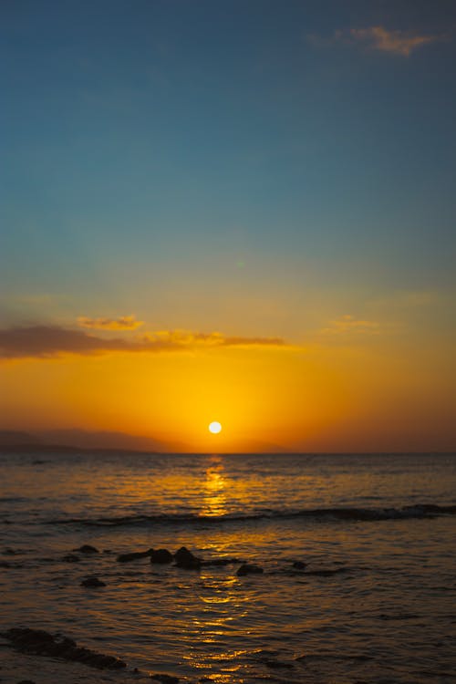 A sunset over the ocean with a rock in the foreground