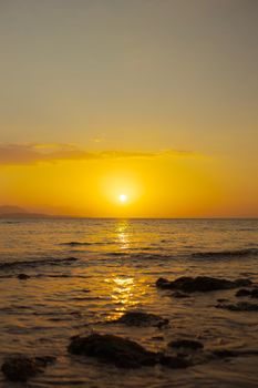 Stunning sunset over a rocky seashore with golden reflections on the water.