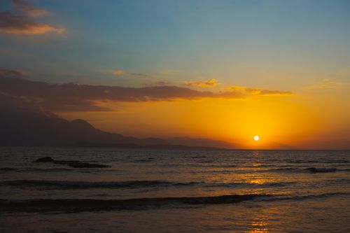Free A beautiful sunset over ocean waves and distant mountains, casting a warm glow. Stock Photo