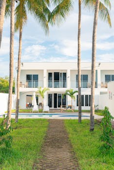 Bright modern villa surrounded by tropical palm trees and a pool, ideal for summer getaways.