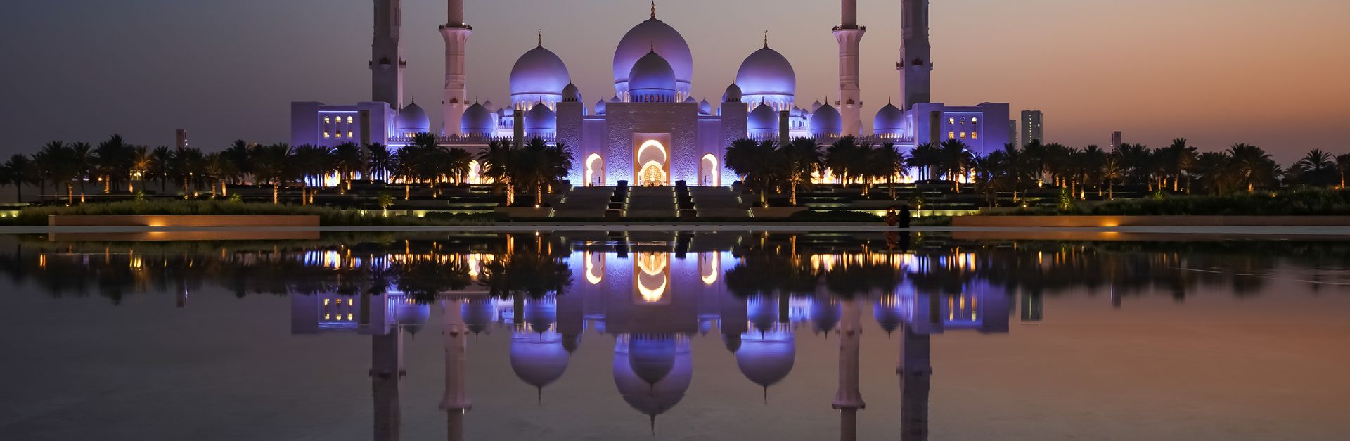 The magnificent Sheikh Zayed Grand Mosque reflecting in serene waters during twilight in Abu Dhabi.