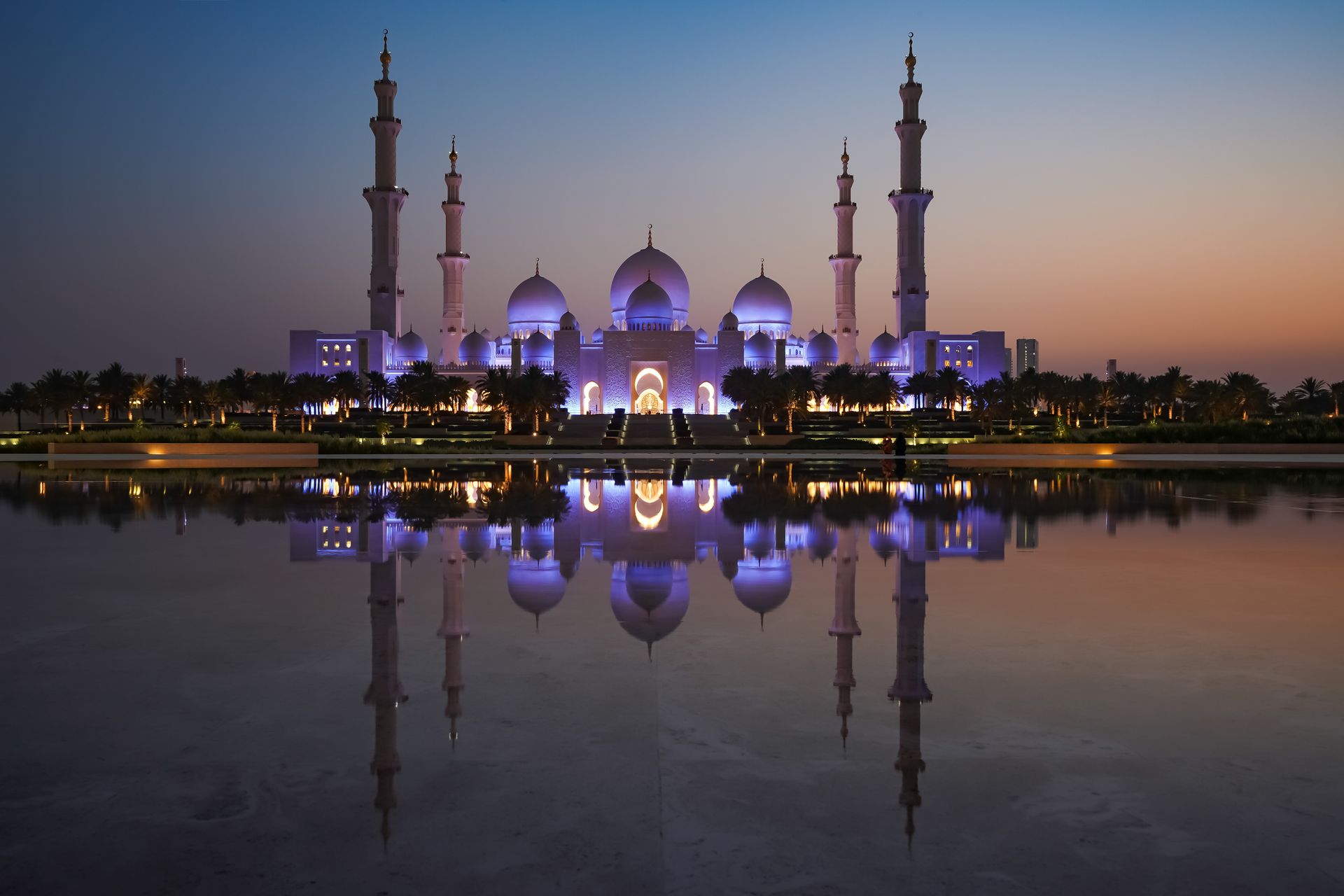 The magnificent Sheikh Zayed Grand Mosque reflecting in serene waters during twilight in Abu Dhabi.