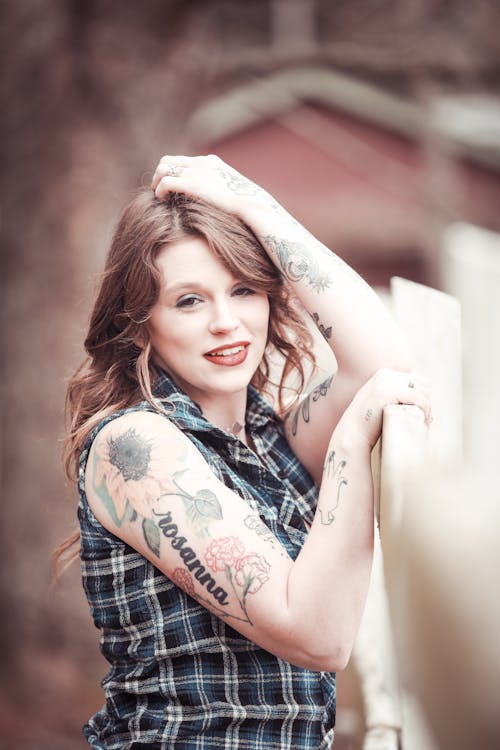 A woman with tattoos leaning against a fence