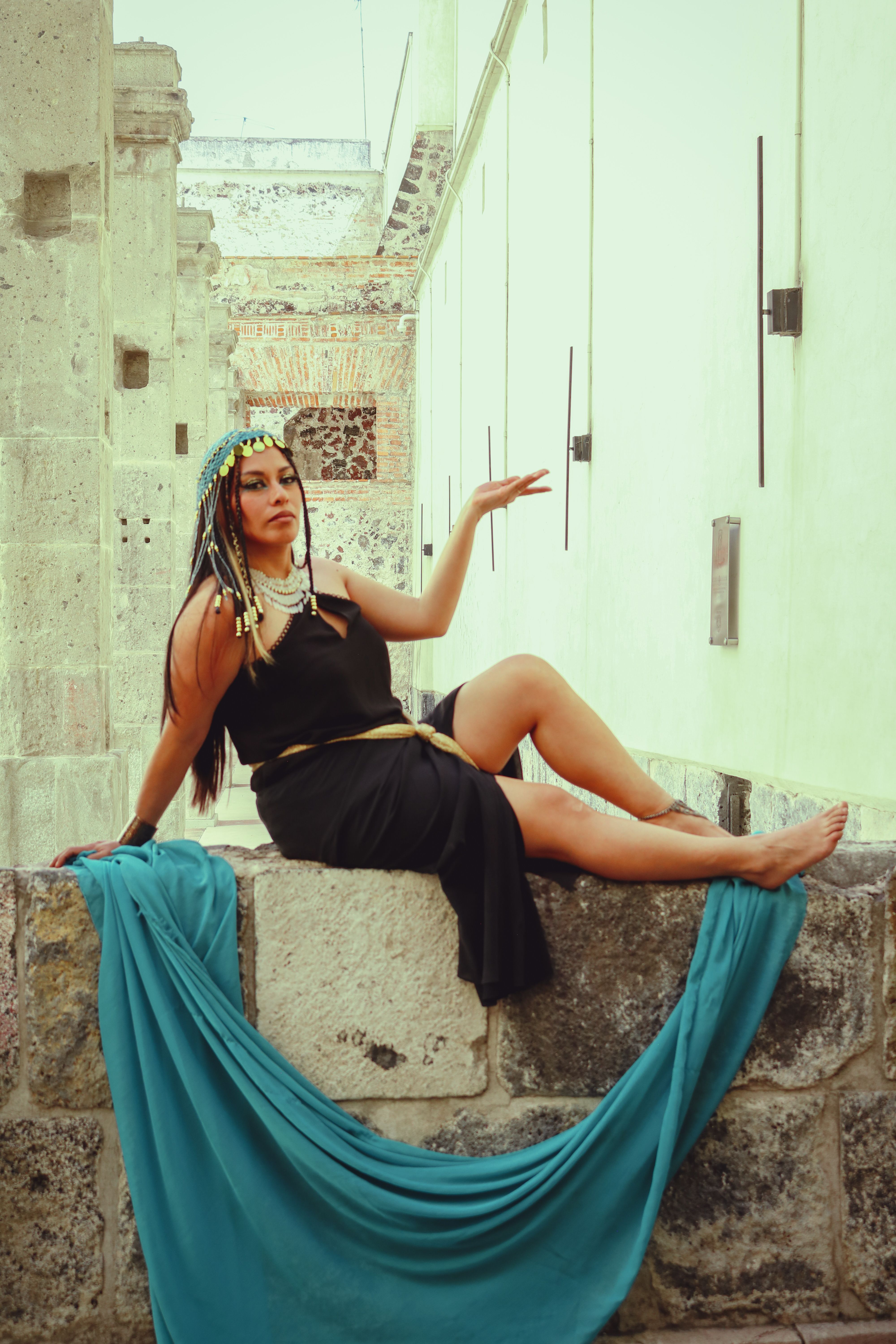 A model in a black dress poses stylishly in an outdoor alley, conveying elegance and fashion.