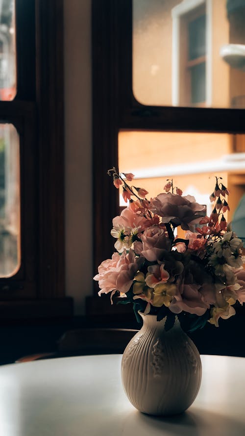 A vase with flowers sitting on a table in front of a window