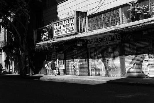 Monochrome photo of an urban street in Mexico City with closed store shutters and shadow play.