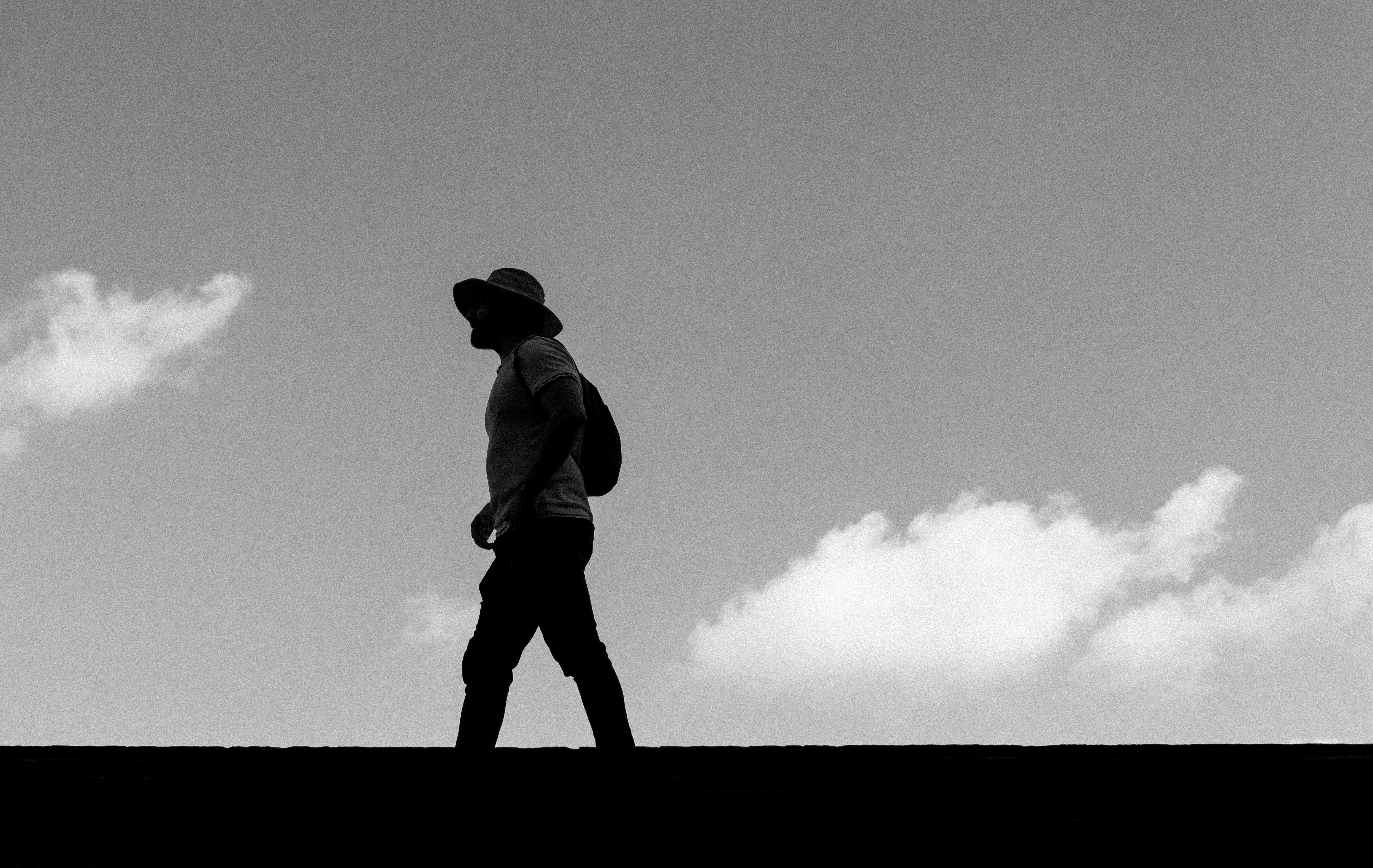 Silhouette of a man walking outdoors against a cloudy sky in black and white.