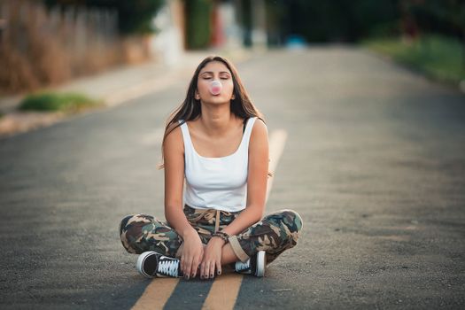 Photo of Sitting in the Middle of the Road With Her Legs Crossed Blowing Bubble Gum