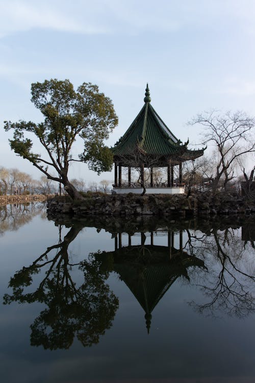 A gazebo sits on the water in front of a tree