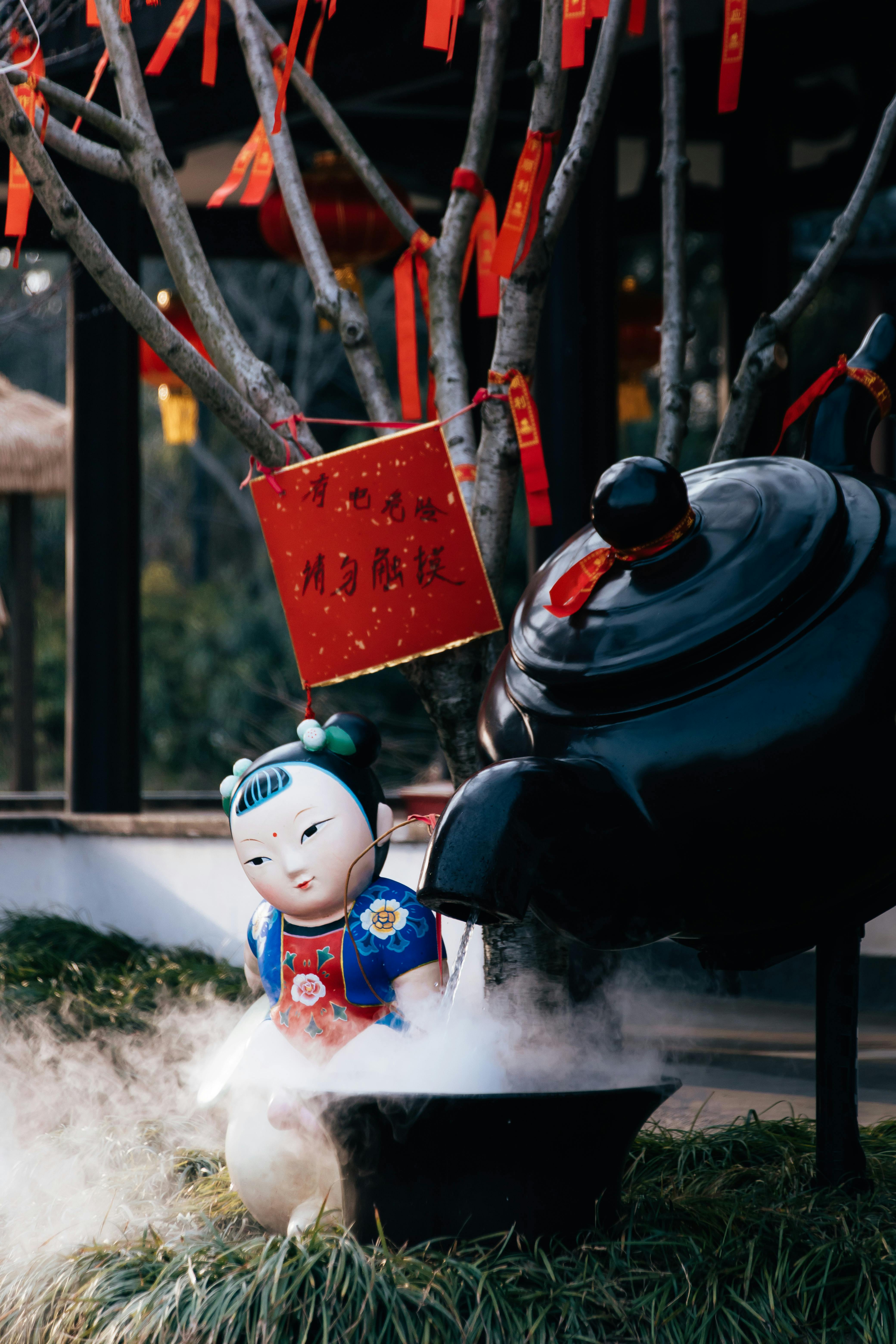 A Chinese figurine with a large teapot and red decorations in an outdoor setting.