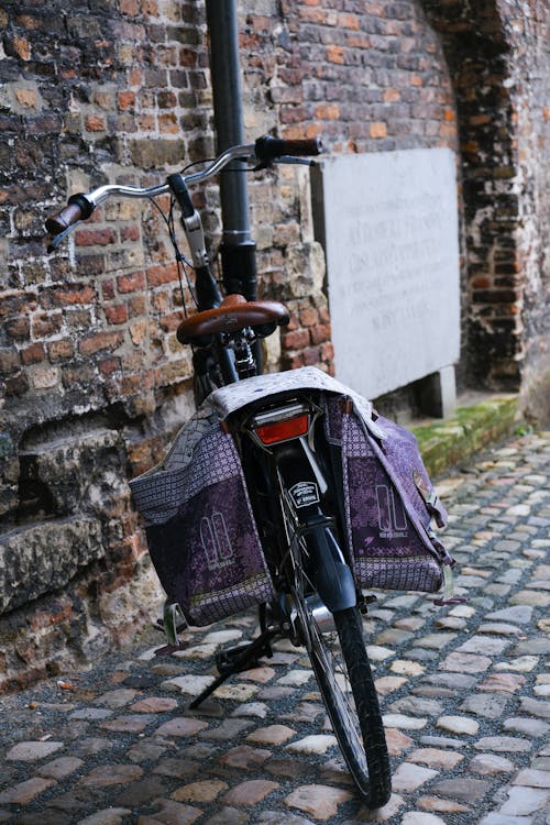 A bicycle parked on a cobblestone street with a purple bag on the back