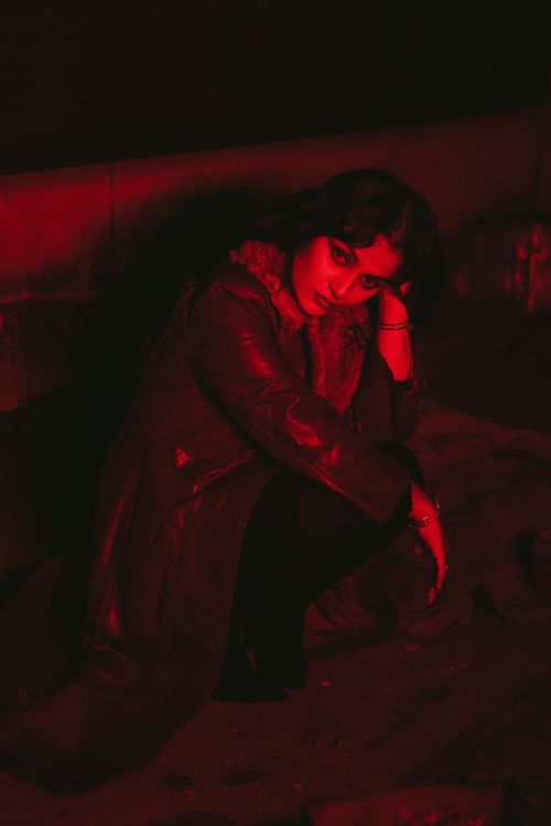 Free Stylish woman posing in a dimly lit urban setting with dramatic red lighting. Stock Photo