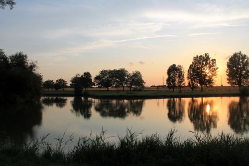 Free Peaceful sunset scene over a calm lake with tree reflections creating a tranquil atmosphere. Stock Photo