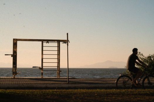 Silhouette of a cyclist riding along a coastal path with mountains in the background at sunset.