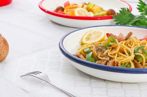 Free Close-up of a delicious pasta meal garnished with lemon slices and vegetables on a dining table. Stock Photo