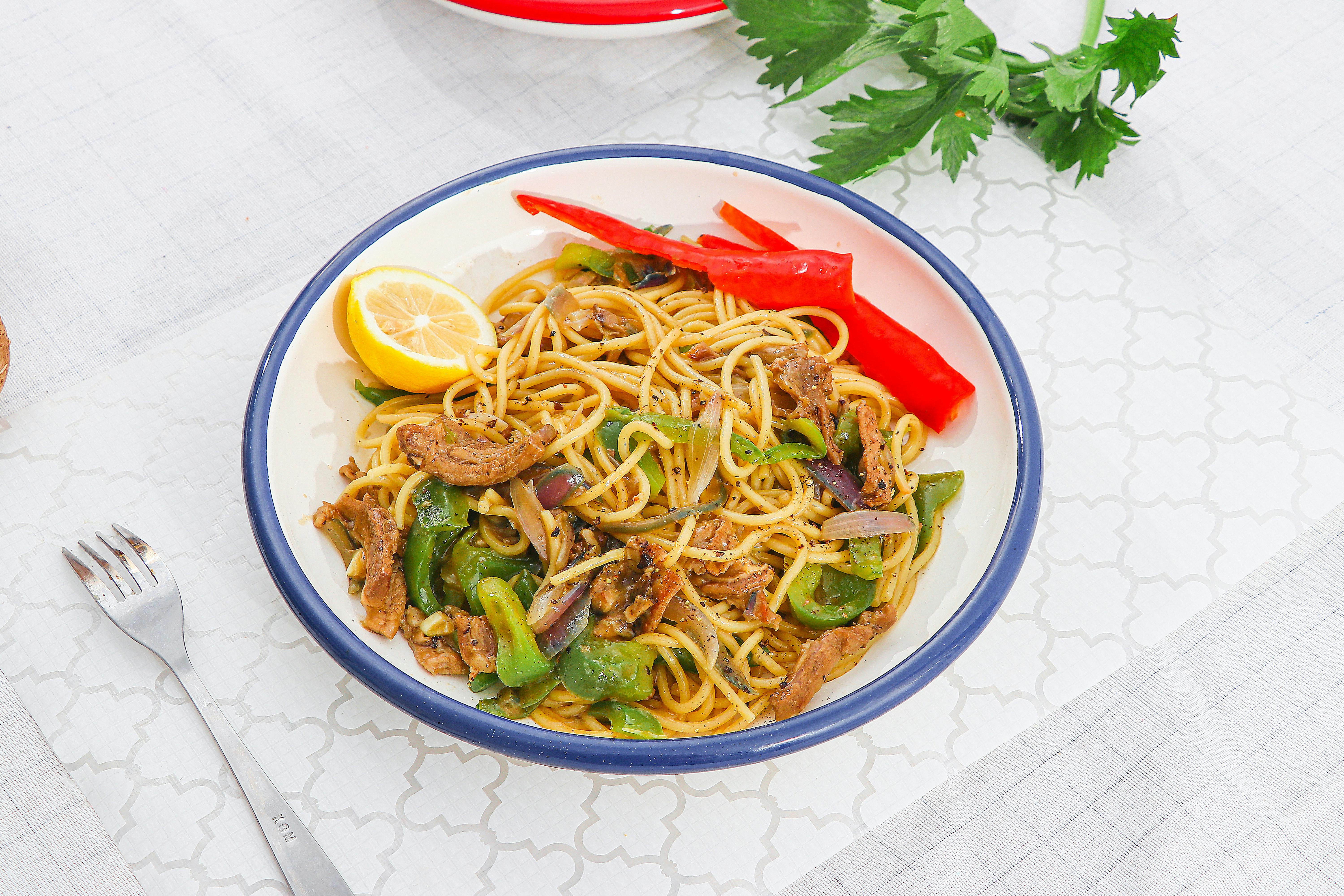 A white plate filled with Nigerian-style spaghetti in tomato sauce with mixed vegetables, showing the characteristic orange-red color from curry powder and scotch bonnet peppers