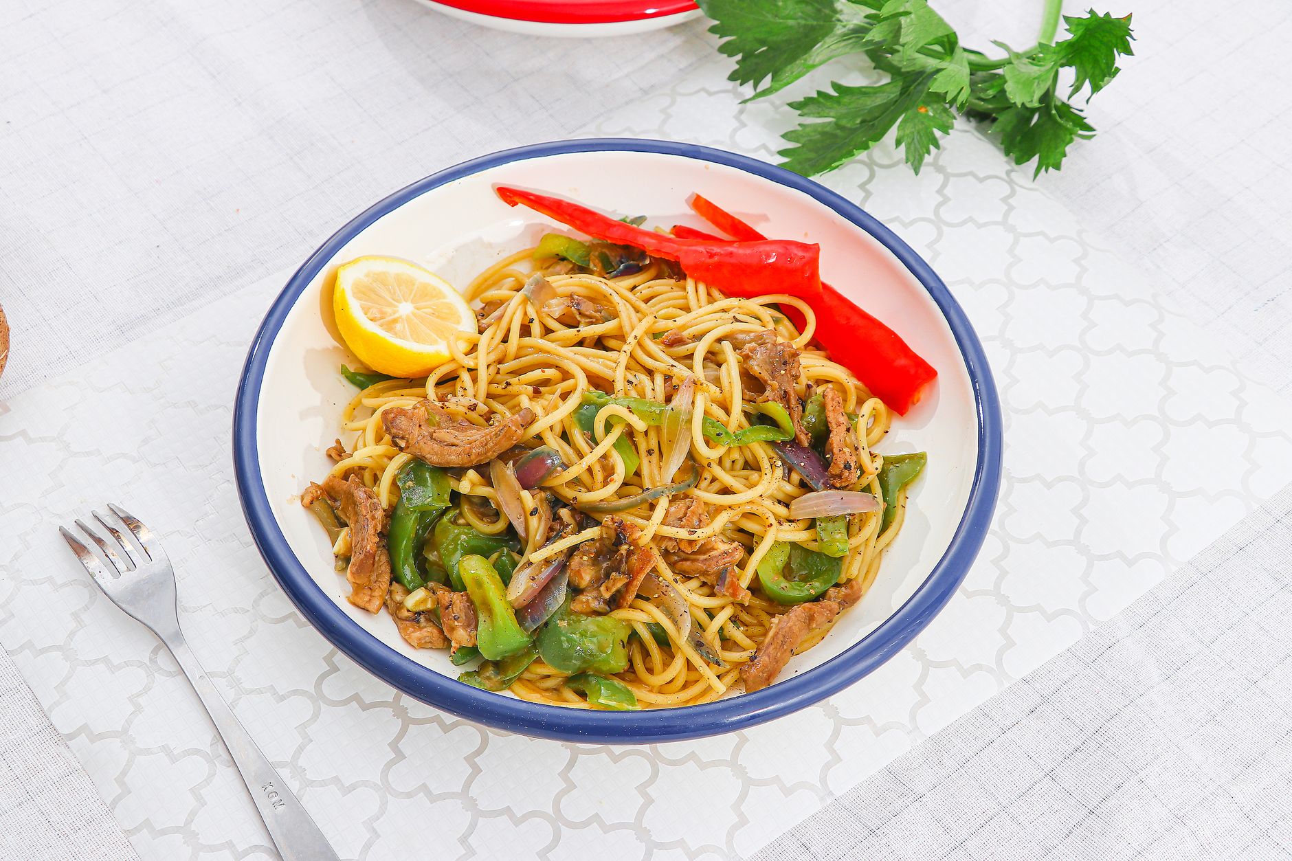 A white plate filled with Nigerian-style spaghetti in tomato sauce with mixed vegetables, showing the characteristic orange-red color from curry powder and scotch bonnet peppers