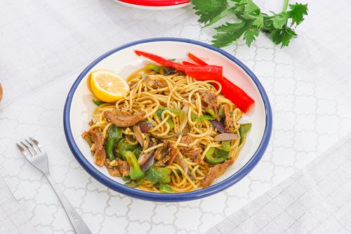 Free Appetizing spaghetti with vegetables, lemon slice, and colorful peppers on a patterned tablecloth. Stock Photo