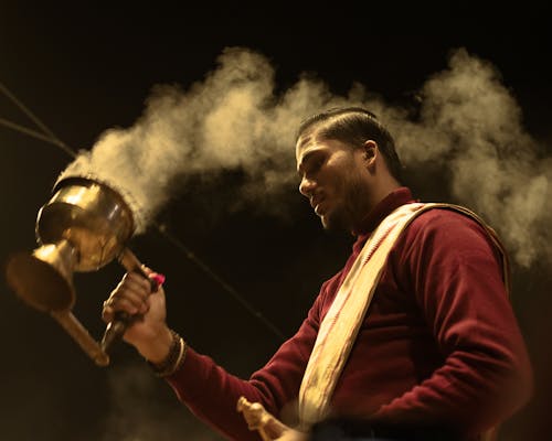 A man is holding a metal pot with smoke coming out of it