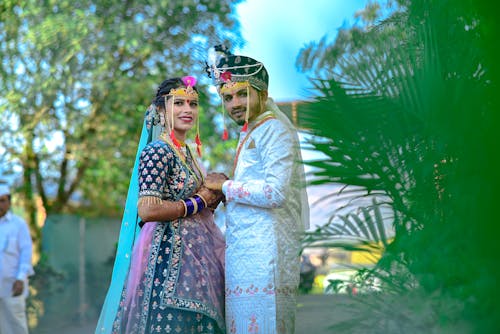 A couple in traditional attire standing in front of trees