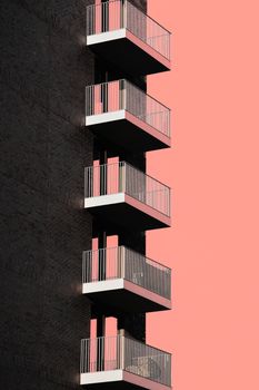 Vertical view of modern balconies set against a bold pink sky. Urban residential architecture with strong geometric lines.