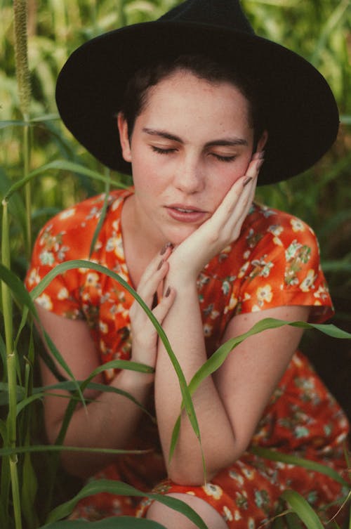 A woman in a hat and dress is sitting in tall grass