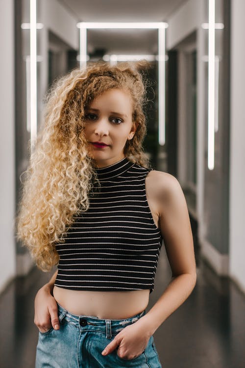 Photo of Woman in Black and White Striped Crop Top Standing in Well Lit Hallway