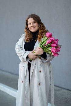 Portrait of a woman with brown hair holding a bouquet of pink tulips against a gray background.