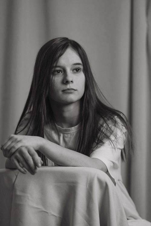 Free Black and white portrait of a teenage girl with long hair, sitting and looking thoughtful. Stock Photo