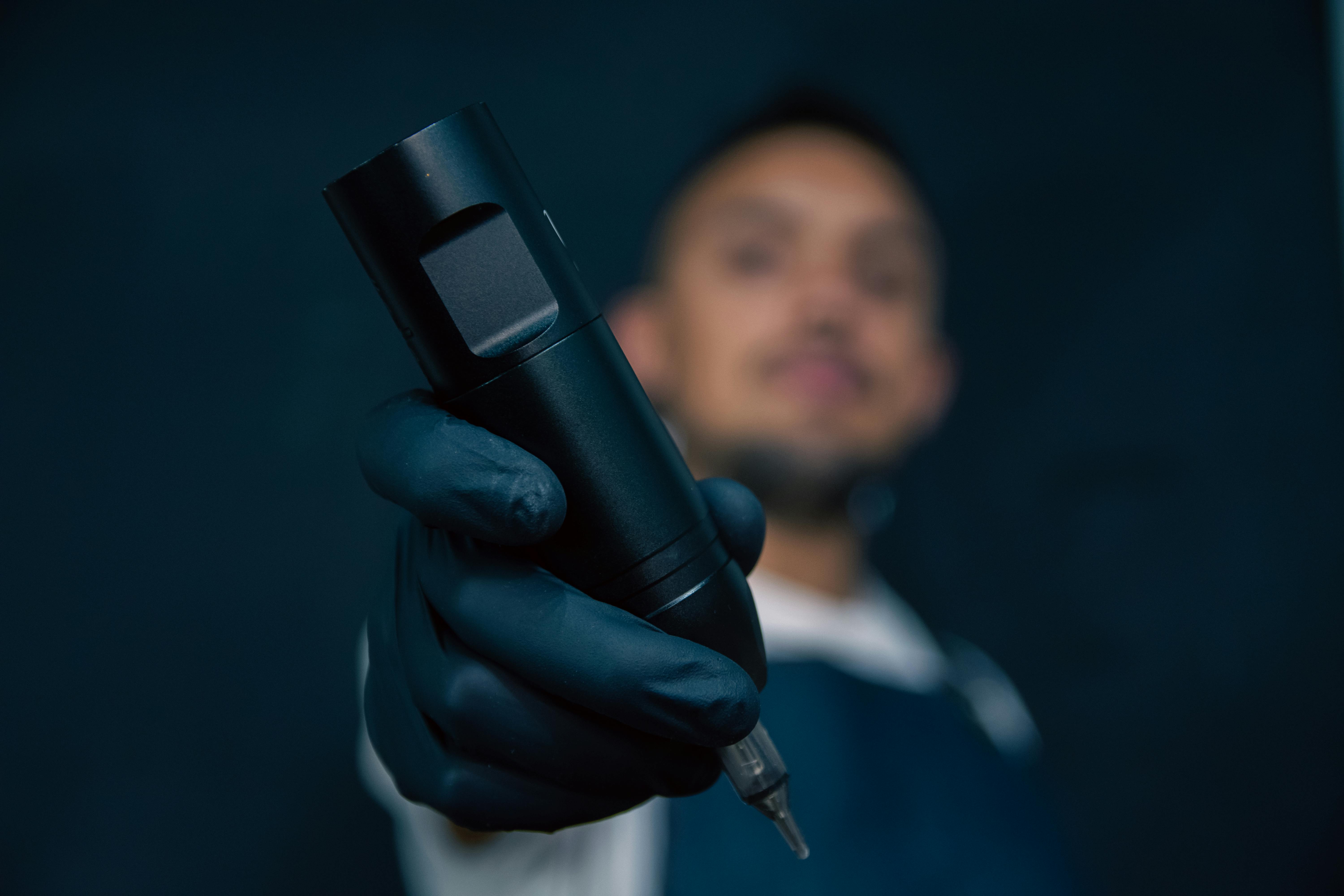 Tattoo artist holding a machine with gloved hand and blurred background.