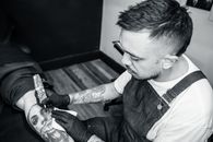 Tattoo artist focused on creating a detailed tattoo on a client's leg in a studio setting.
