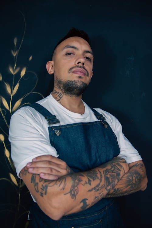 A man with tattoos standing in front of a wall