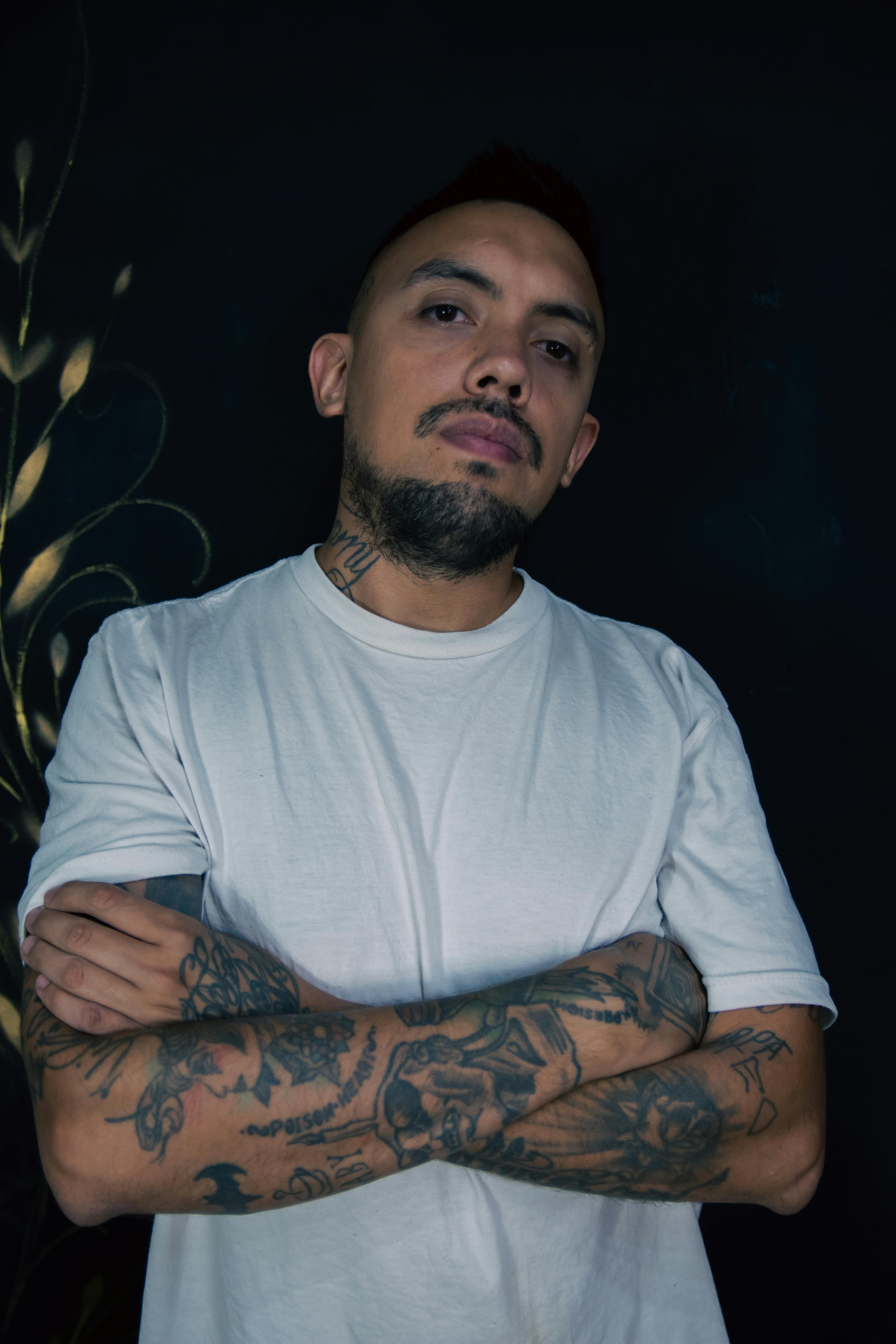Portrait of a confident tattooed man with beard and mustache, posing with crossed arms.
