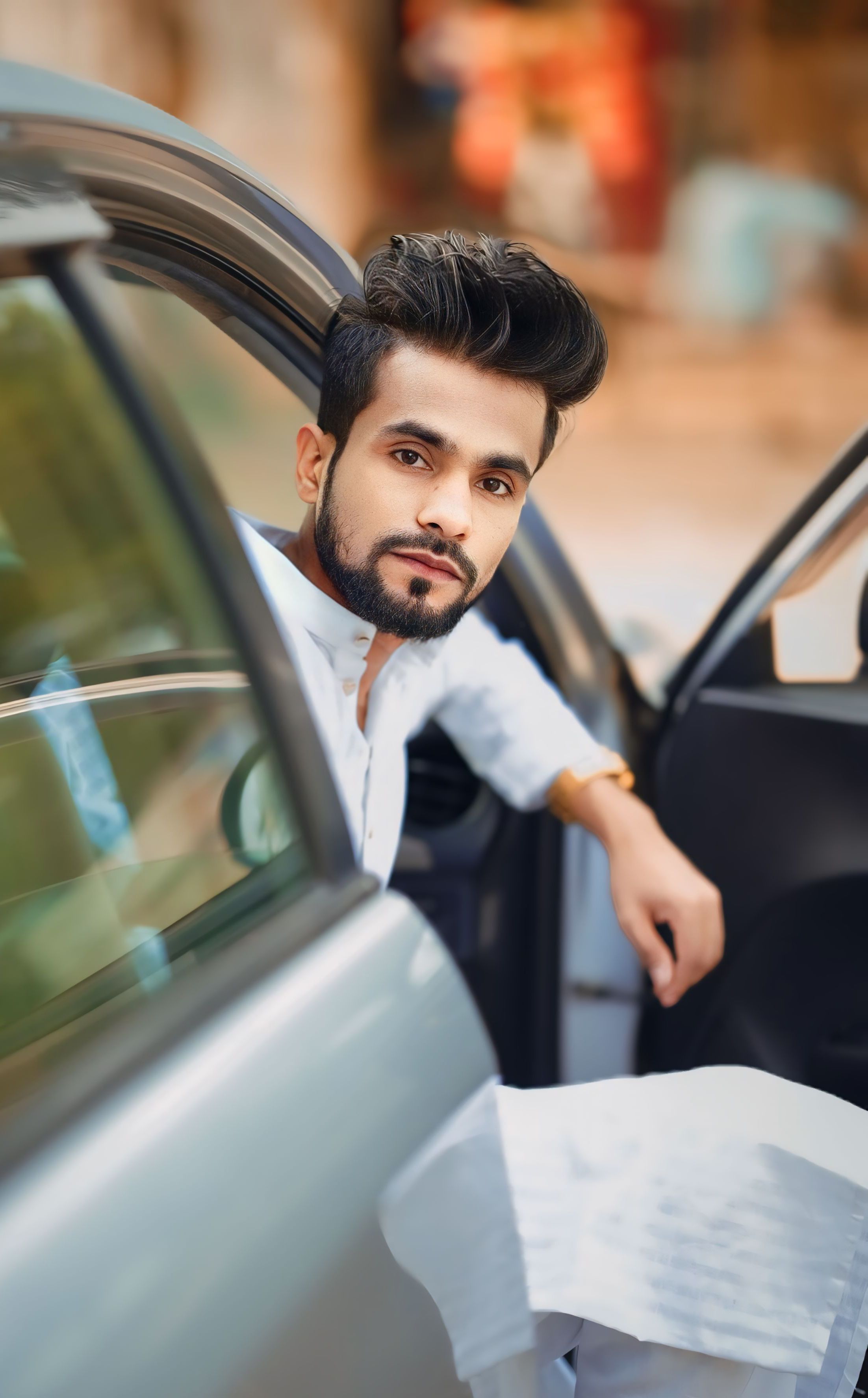 Fashionable man with black hair and beard in a car doorway, highlighting modern style.
