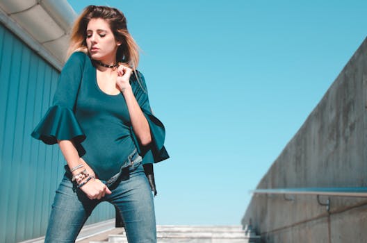 Stylish woman in bodysuit and jeans posing confidently outdoors under a clear blue sky.
