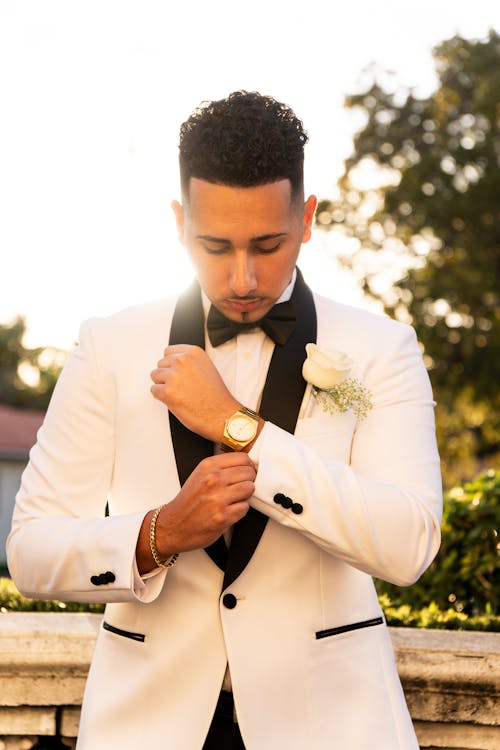 Young Man in a White Tuxedo with Black Lapels Buttoning His Shirt Cuff