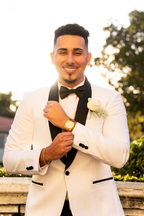 Free A groom in a white tuxedo smiling in an outdoor setting, exuding joy and confidence. Stock Photo