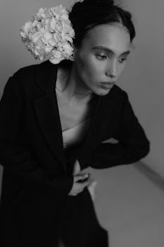 Black and white portrait of a woman in a coat with white flowers, showcasing elegance and fashion.