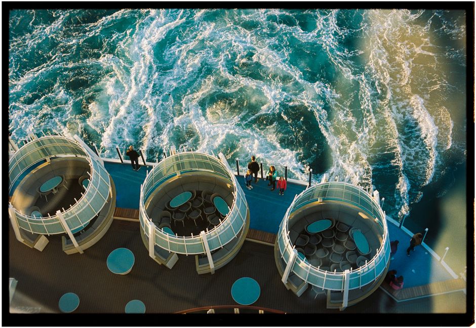 Aerial shot of cruise ship deck, showcasing round seating areas and ocean waves.