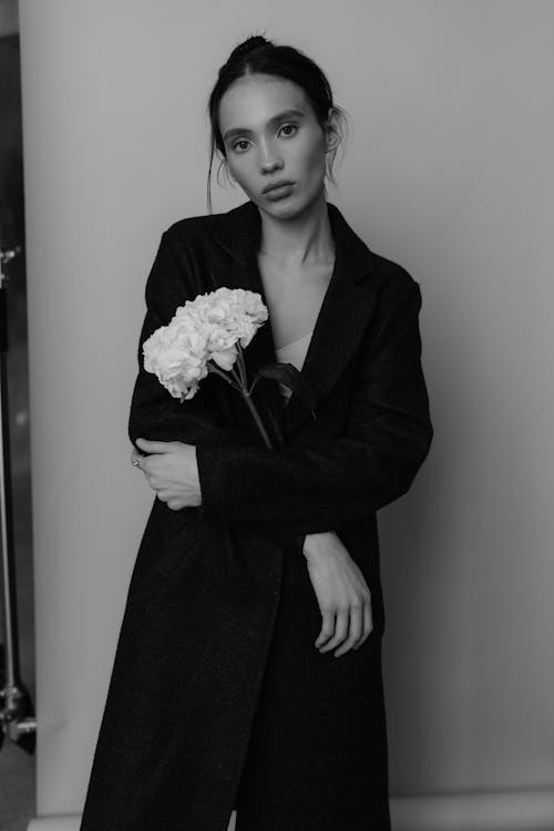 A woman in a black coat holding a flower