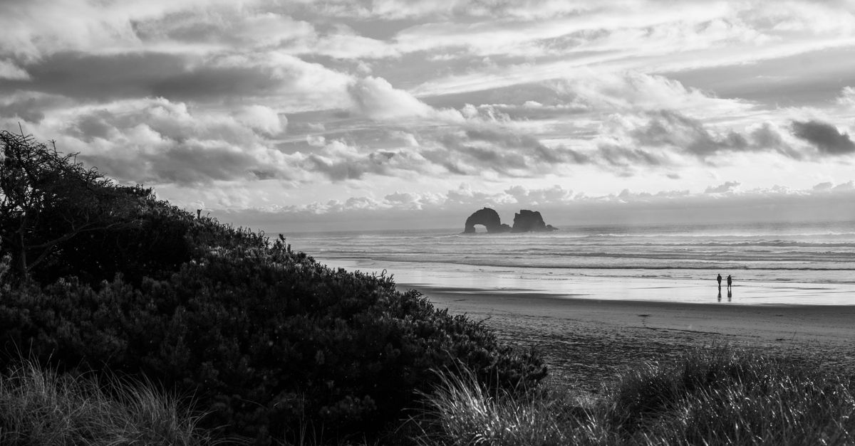 Explore the serene beauty of Rockaway Beach with its iconic natural arch in a stunning black and white setting.