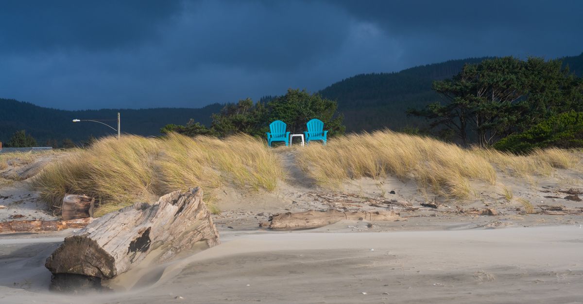 Empty chairs on Rockaway Beach, Oregon, under dramatic skies and windswept dunes.